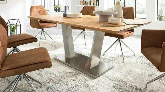 Moderne Essgruppe mit hellem Holztisch, auffälligem Metallfuß und braunen Polsterstühlen auf einem Teppich.