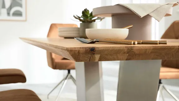 Detailansicht der abgeschrägten Schweizer Kante einer hellen Holztischplatte mit Besteck im Vordergrund.